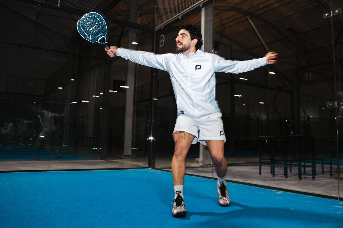 Padel player smashing with a Pallap racket on an indoor blue court