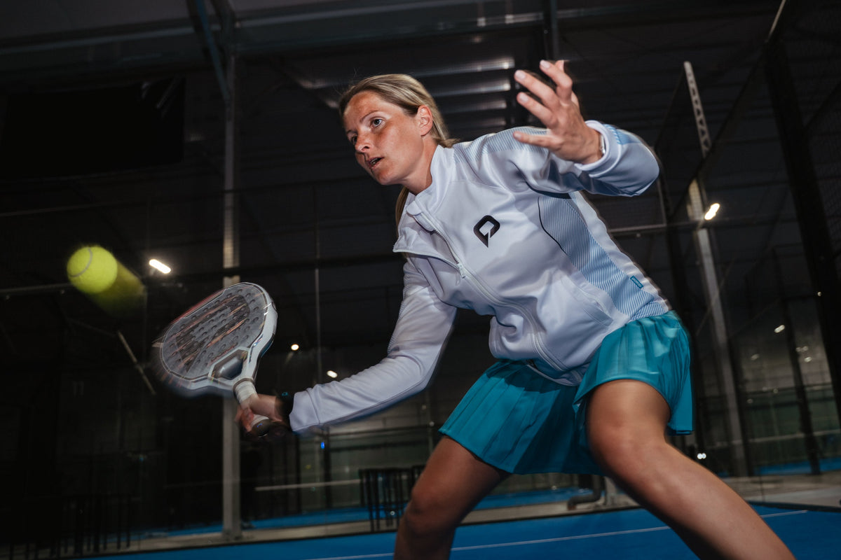 Woman playing a low volley in Pallap jacket and skort on an indoor court