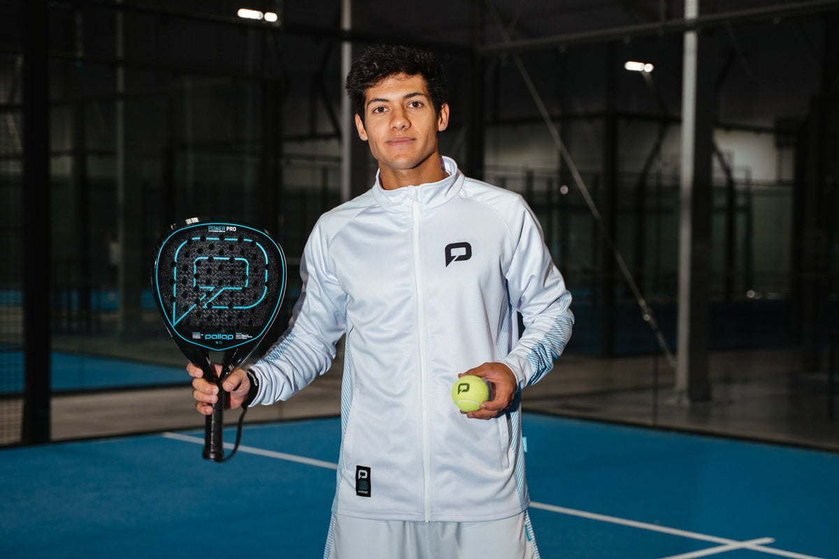 Player in a Pallap padel jacket holding a racket and ball on an indoor court